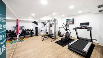 Un gimnasio moderno con cinta de correr, elíptica, banco de pesas y varios mancuernas.