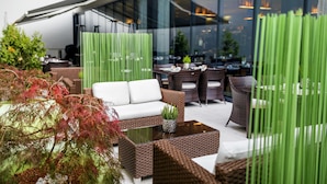 An outdoor seating area with wicker furniture, a glass table, and green decorative panels. - Occidental Praha Five (Prague)