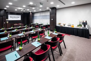 Una sala conferenze con lunghe tavolate, sedie rosse e uno schermo per presentazioni.