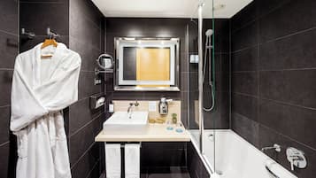 A modern bathroom with a large bathtub, a glass-enclosed shower, a wooden vanity with a sink, and a robe hanging on a rack.