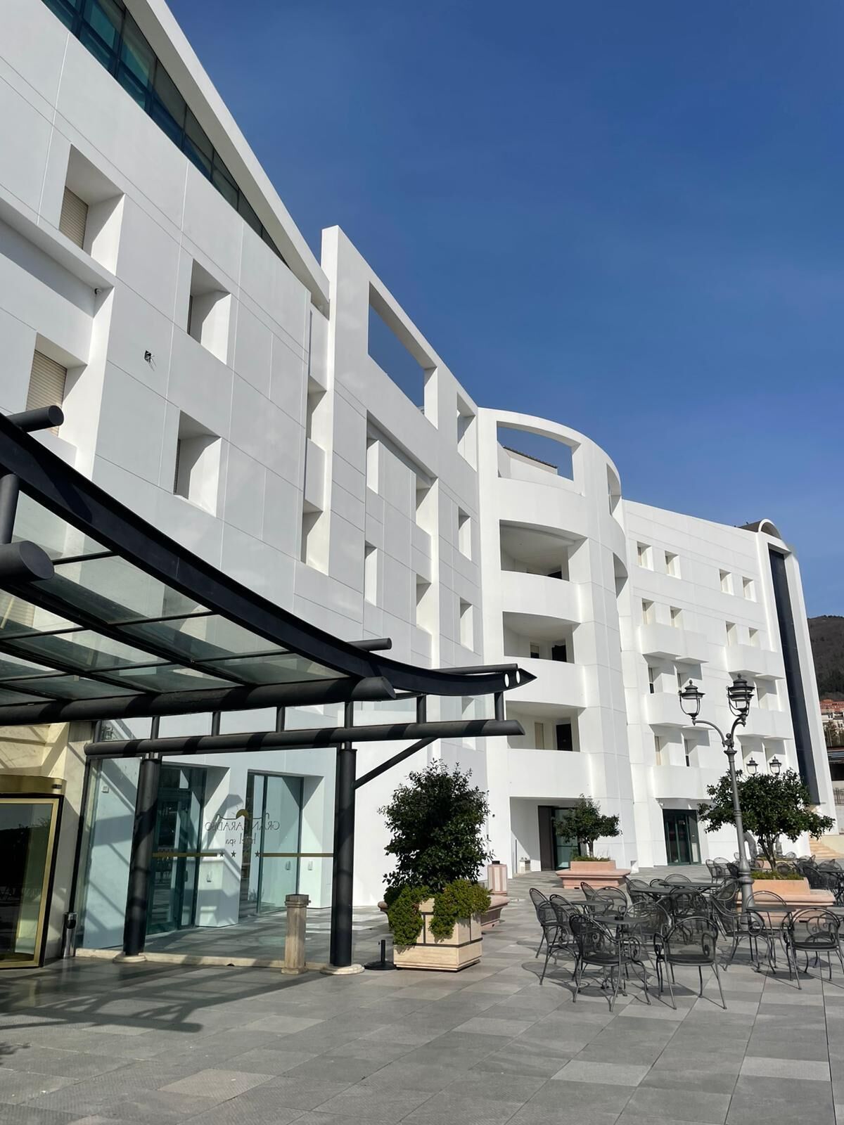 A modern building with a glass entrance, outdoor seating area, and a clear sky.