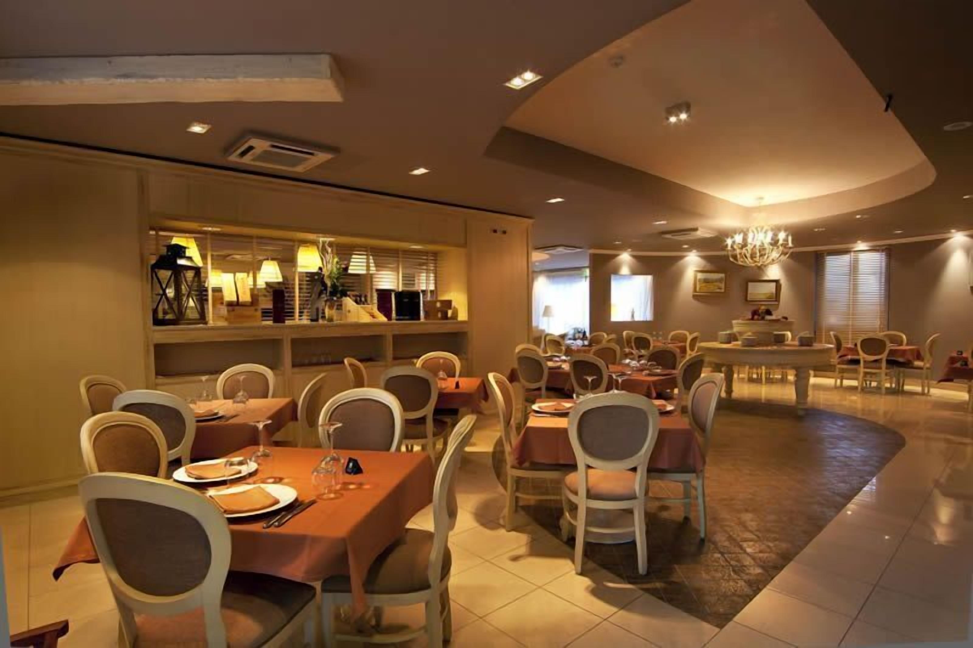 A spacious dining area with multiple tables and chairs, a central bar area, and a chandelier.