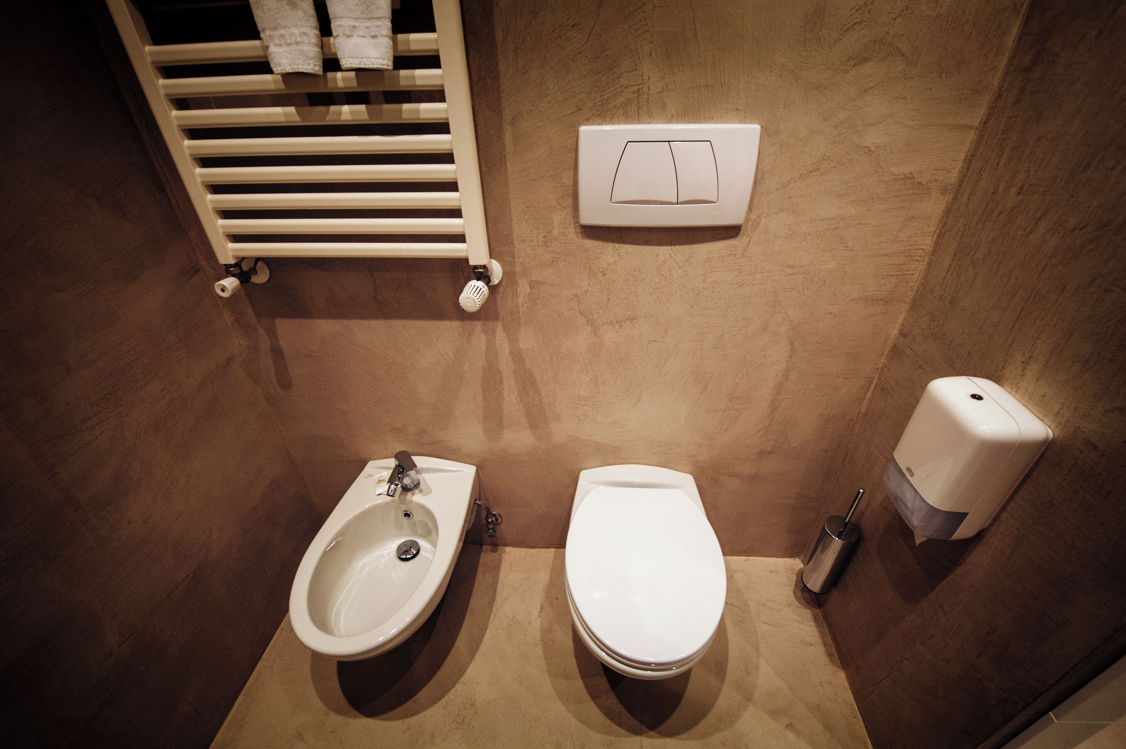 Un bagno con bidet, water, lavandino, portasciugamani e dispenser per sapone.