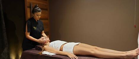 En massageterapi-session i et rum med træpaneler og en massagestol.