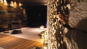 Un interior moderno con pared de piedra, suelo de madera y una zona de estar con una silla y una mesita.