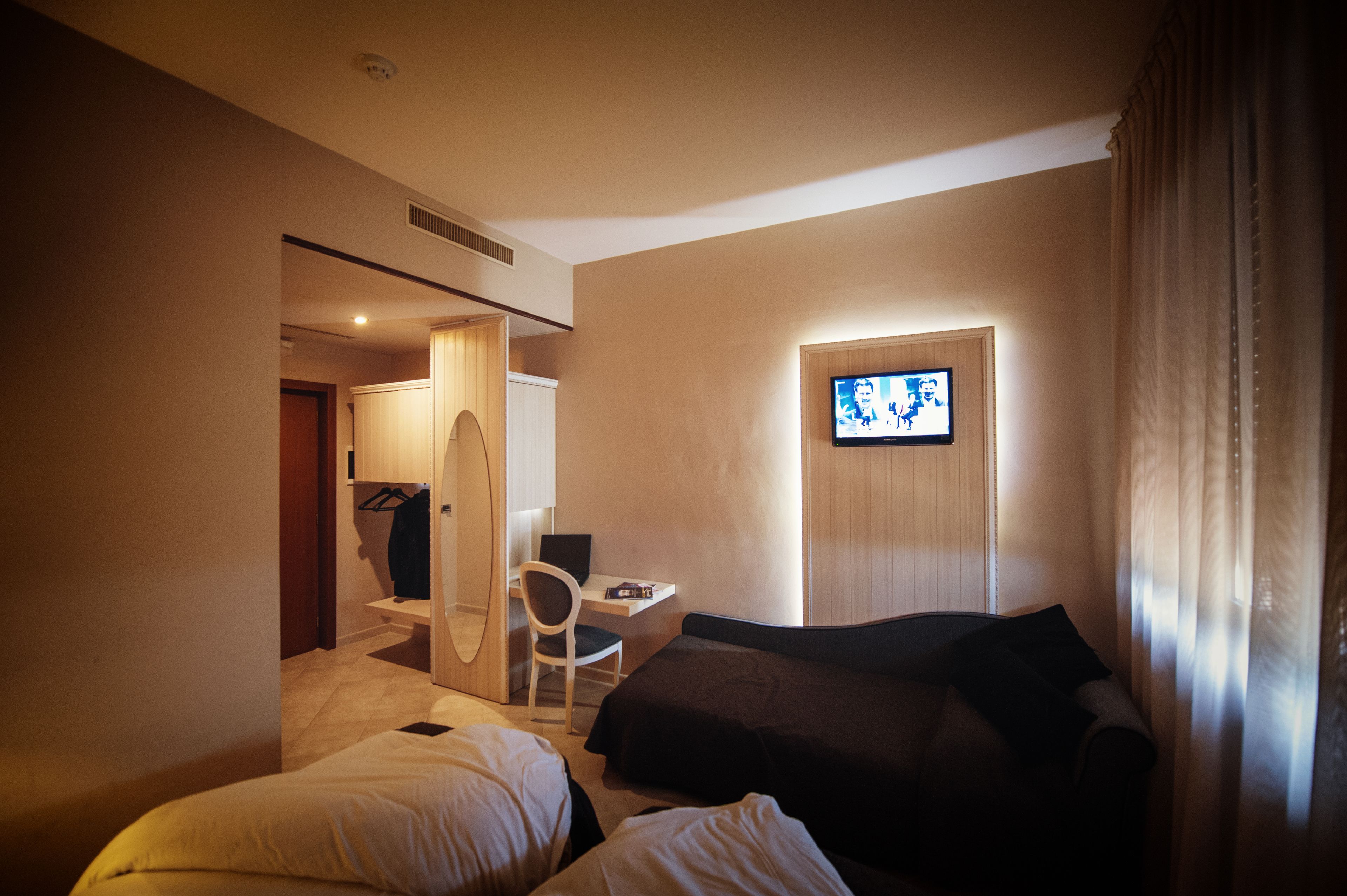 A hotel room with a bed, a desk with a chair, a television, and a wardrobe.