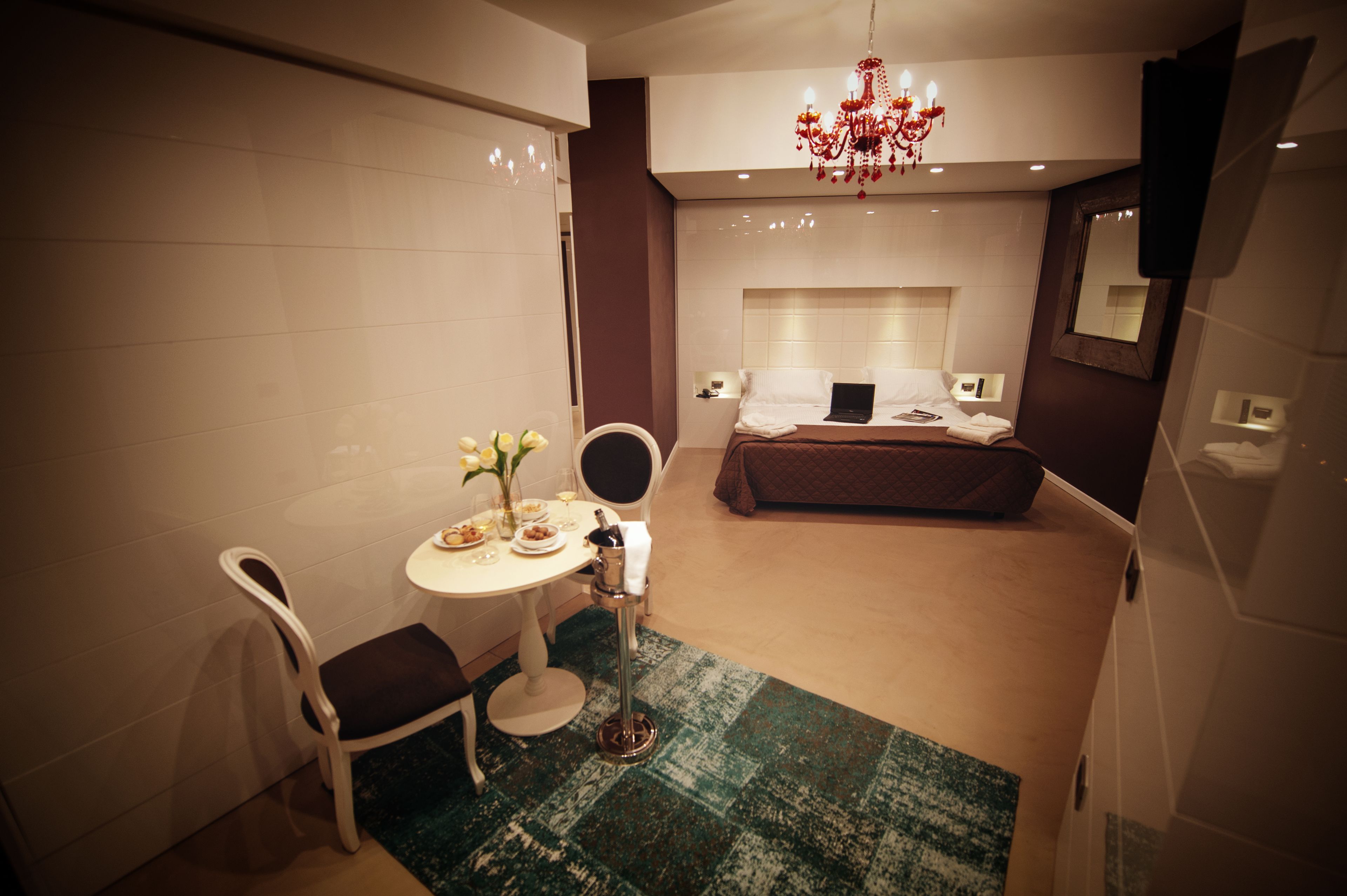 Une chambre d’hôtel avec un lit, un bureau et une chaise, une petite table avec un vase et un lustre.