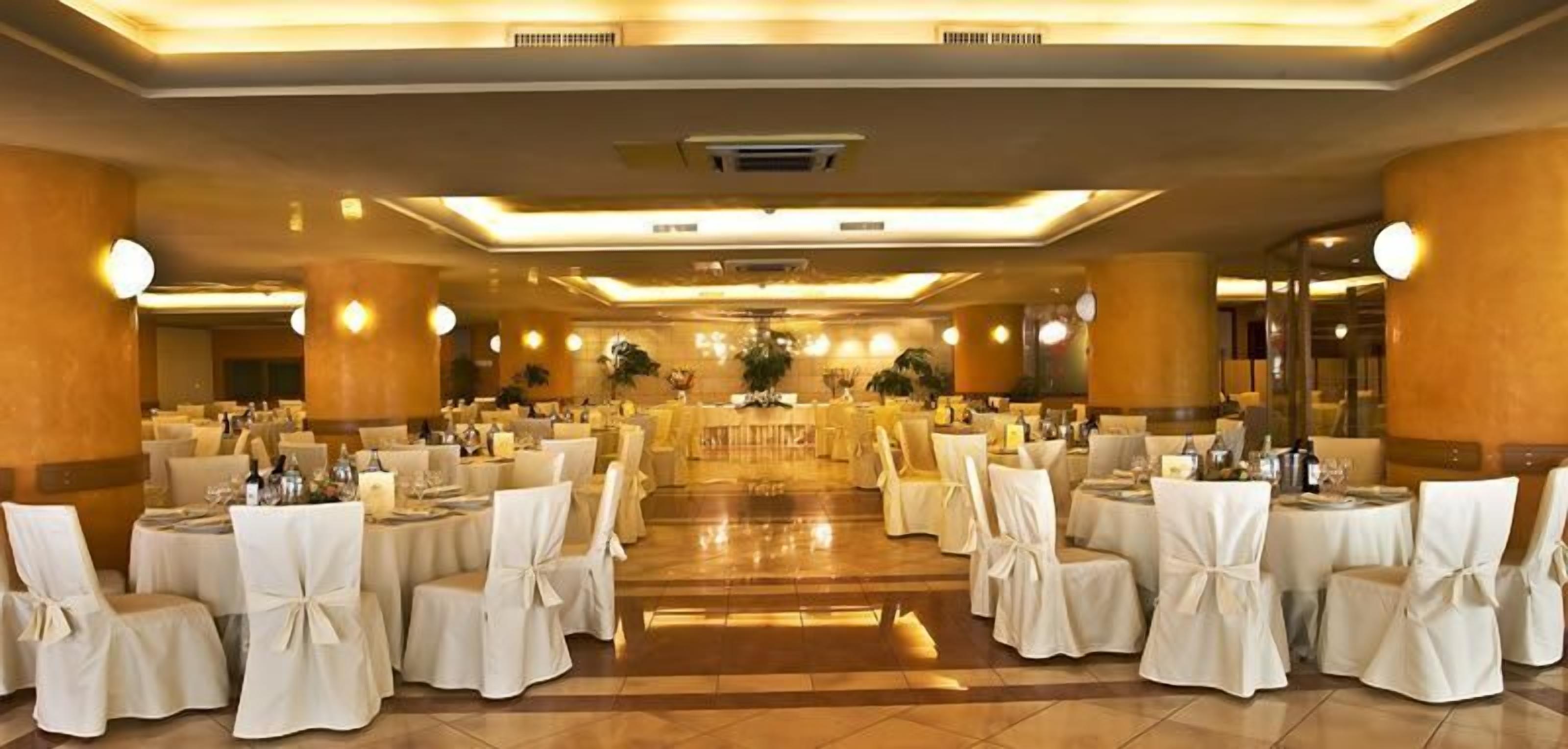 Une salle de banquet avec des tables rondes et des chaises, un arrangement floral central et un plancher ciré.