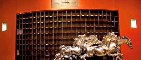 Un vestíbulo de hotel con una gran escultura metálica ornamentada de caballos y una cuadrícula de botellas de vino en la pared.