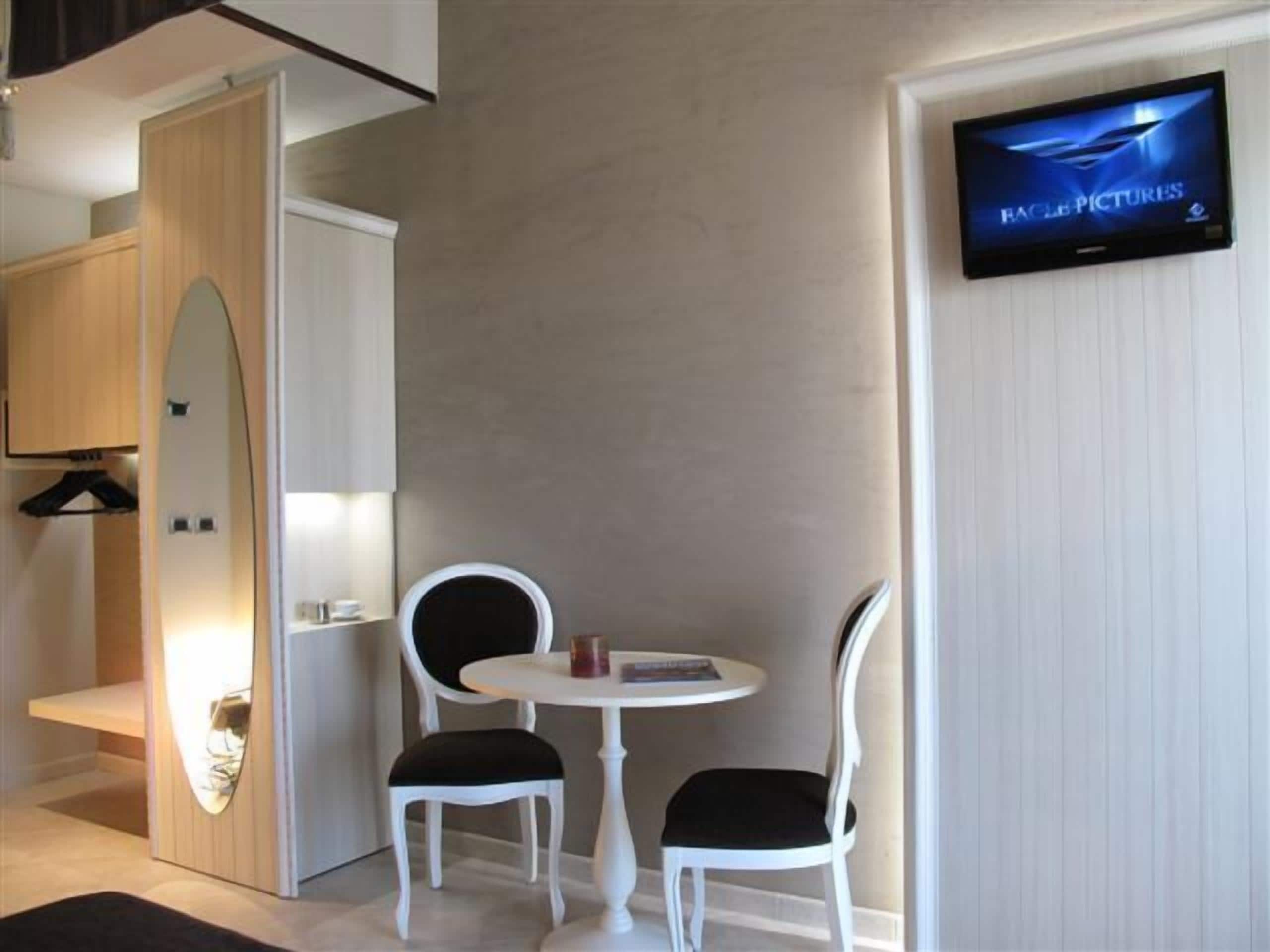 A hotel room with a TV on the wall, two chairs, a small table, and a wardrobe.