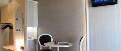 A hotel room with a TV on the wall, two chairs, a small table, and a wardrobe.