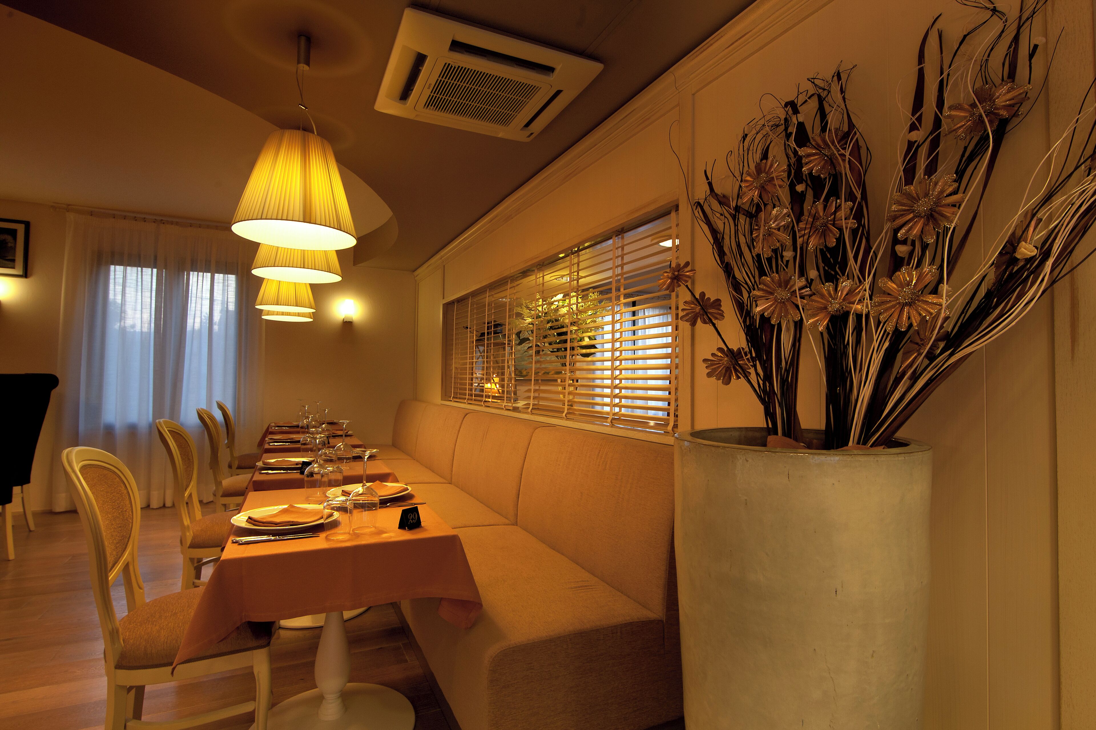 Un comedor con una mesa larga, sillas y un sofá. Hay un jarrón grande con plantas secas sobre la mesa.