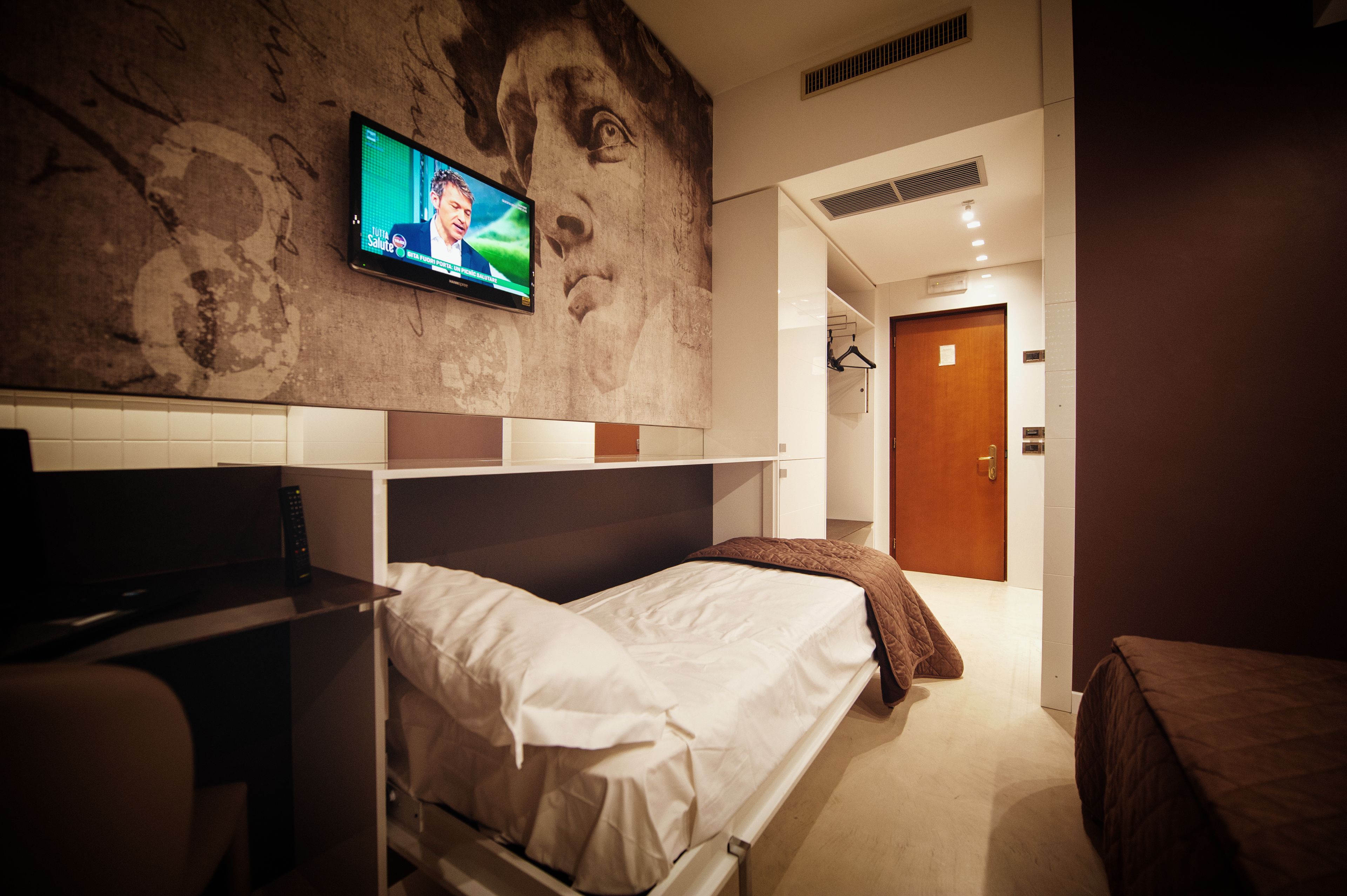 Une chambre d’hôtel avec un lit, un téléviseur fixé au mur et une porte donnant sur une autre pièce.