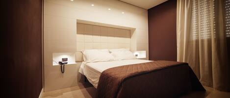 A modern bedroom with a bed, bedside tables, and a wall-mounted light fixture.