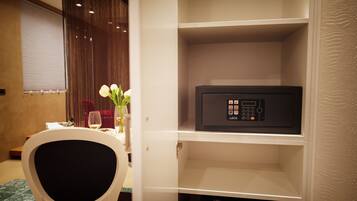 A hotel room with a white cabinet containing a black microwave, a dining table with a vase of white flowers, and a chair.
