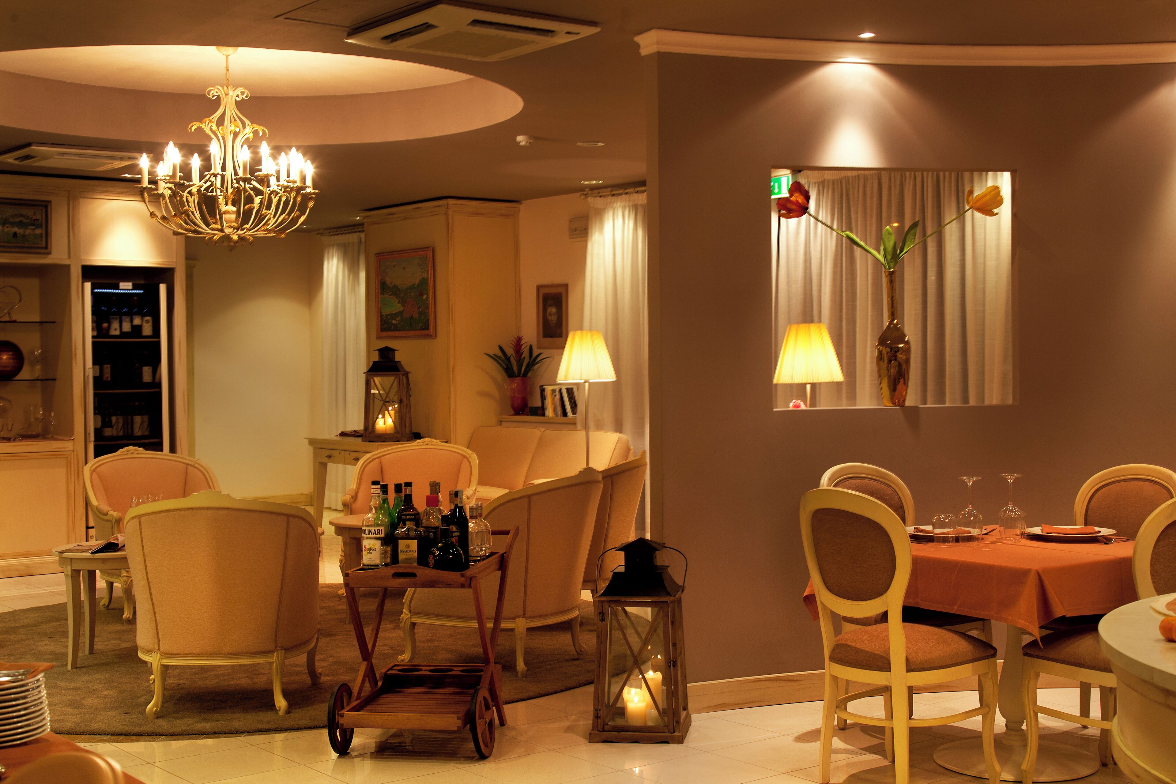 A dining area with a chandelier, chairs, a table set for four, and a bar area with bottles.