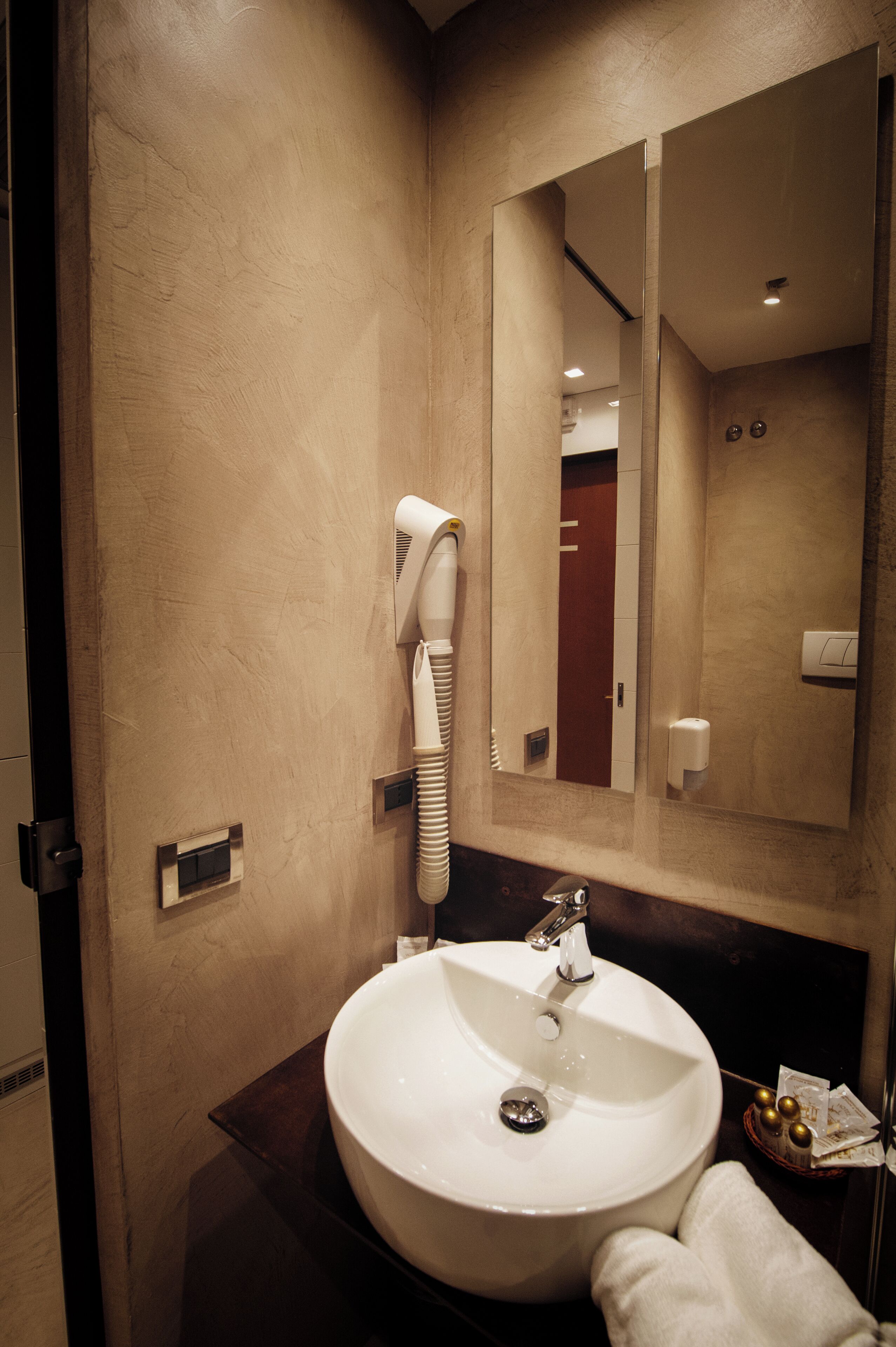 A bathroom with a round sink, a hairdryer mounted on the wall, and a mirror above the sink.
