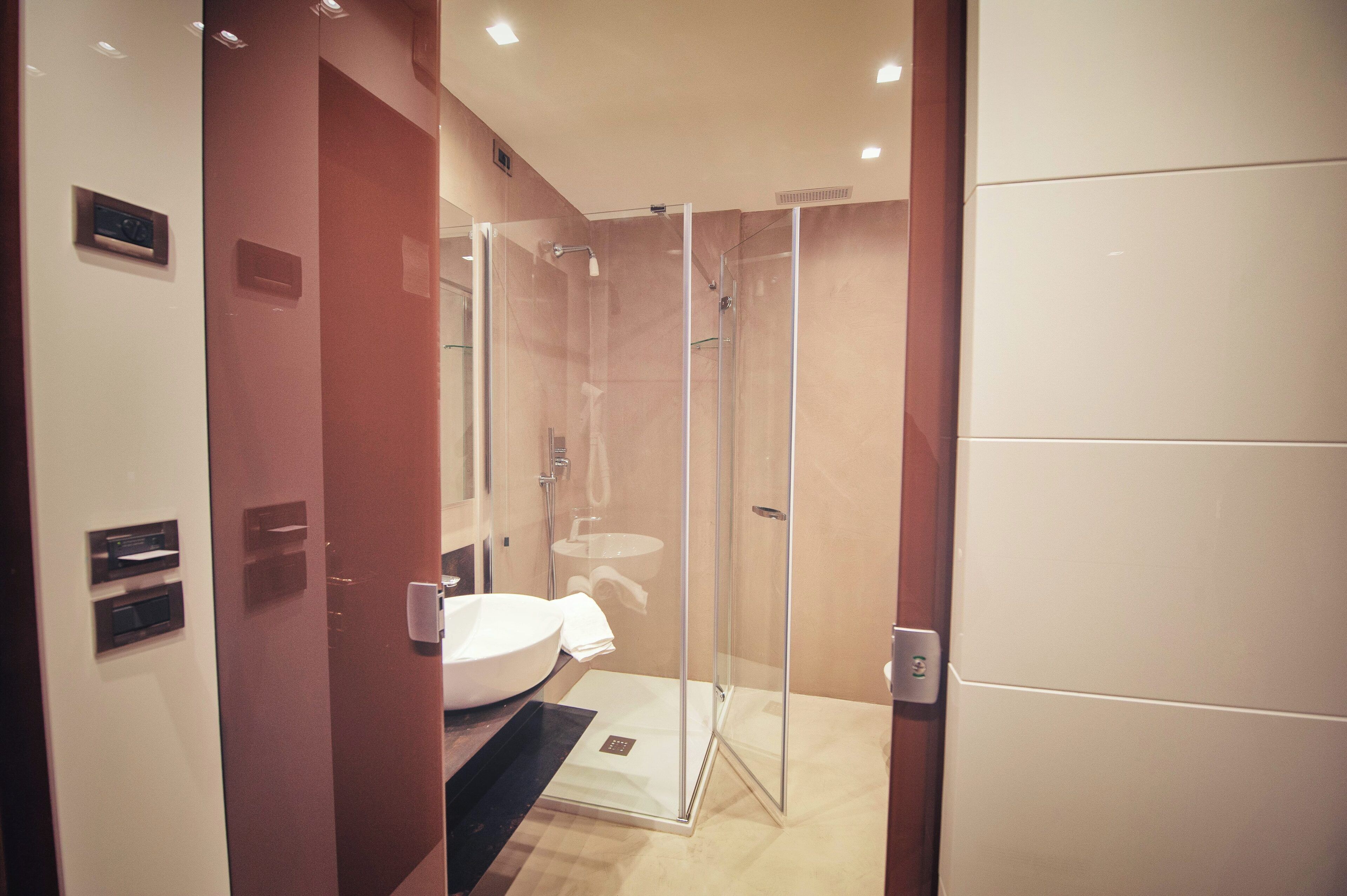 A modern bathroom with a glass-enclosed shower, a white sink, and a wooden floor.