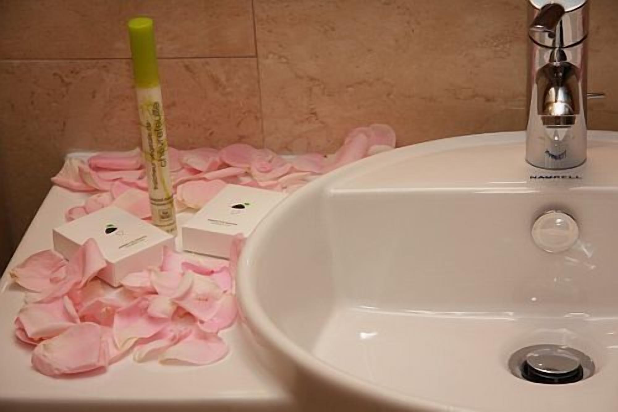 Un lavamanos con un espejo, una botella verde y dos cajas blancas sobre una toalla rosa.