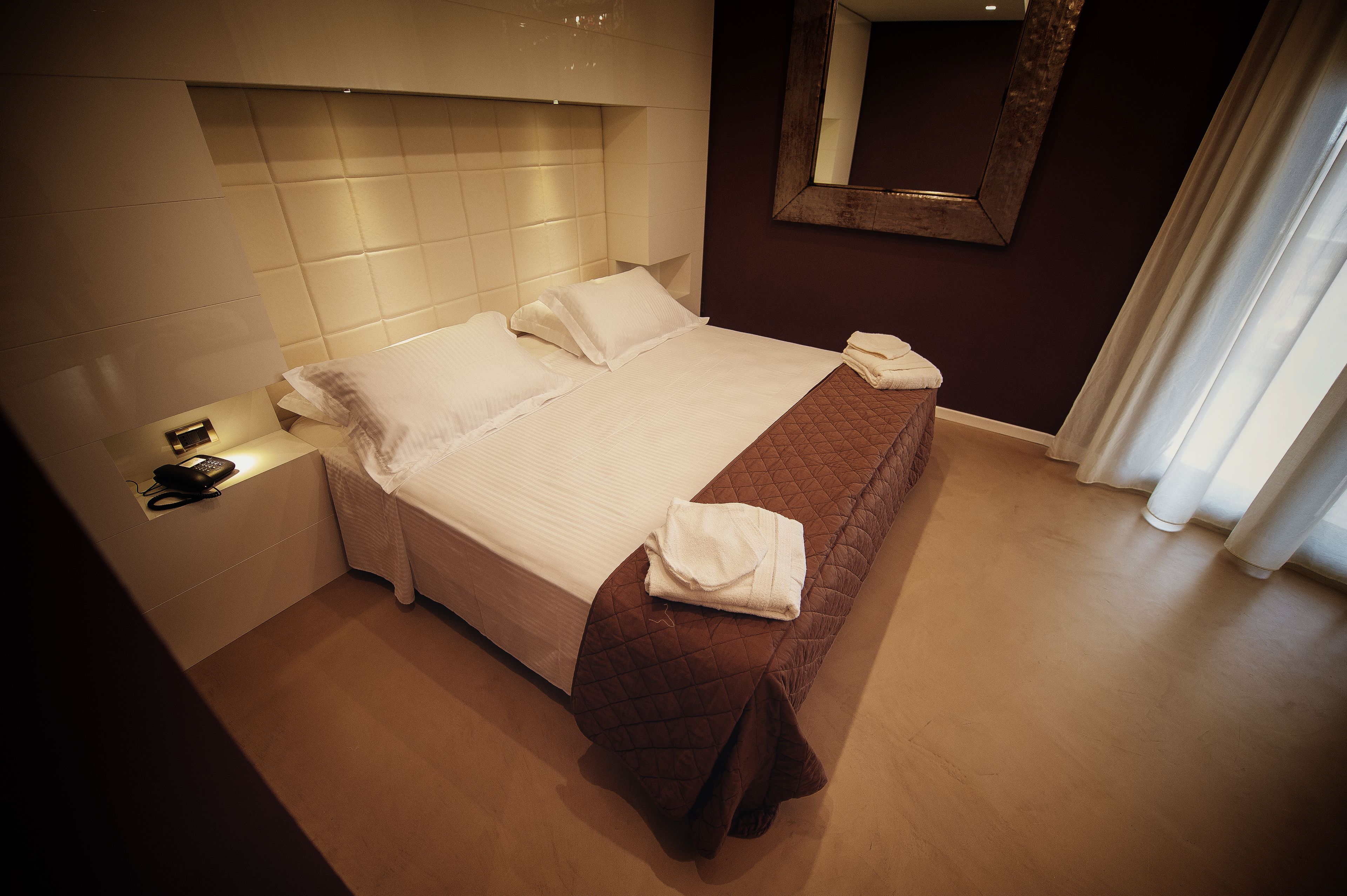 Un lit bien fait, avec une couverture marron, du linge de lit blanc et une serviette pliée posée sur le côté.
