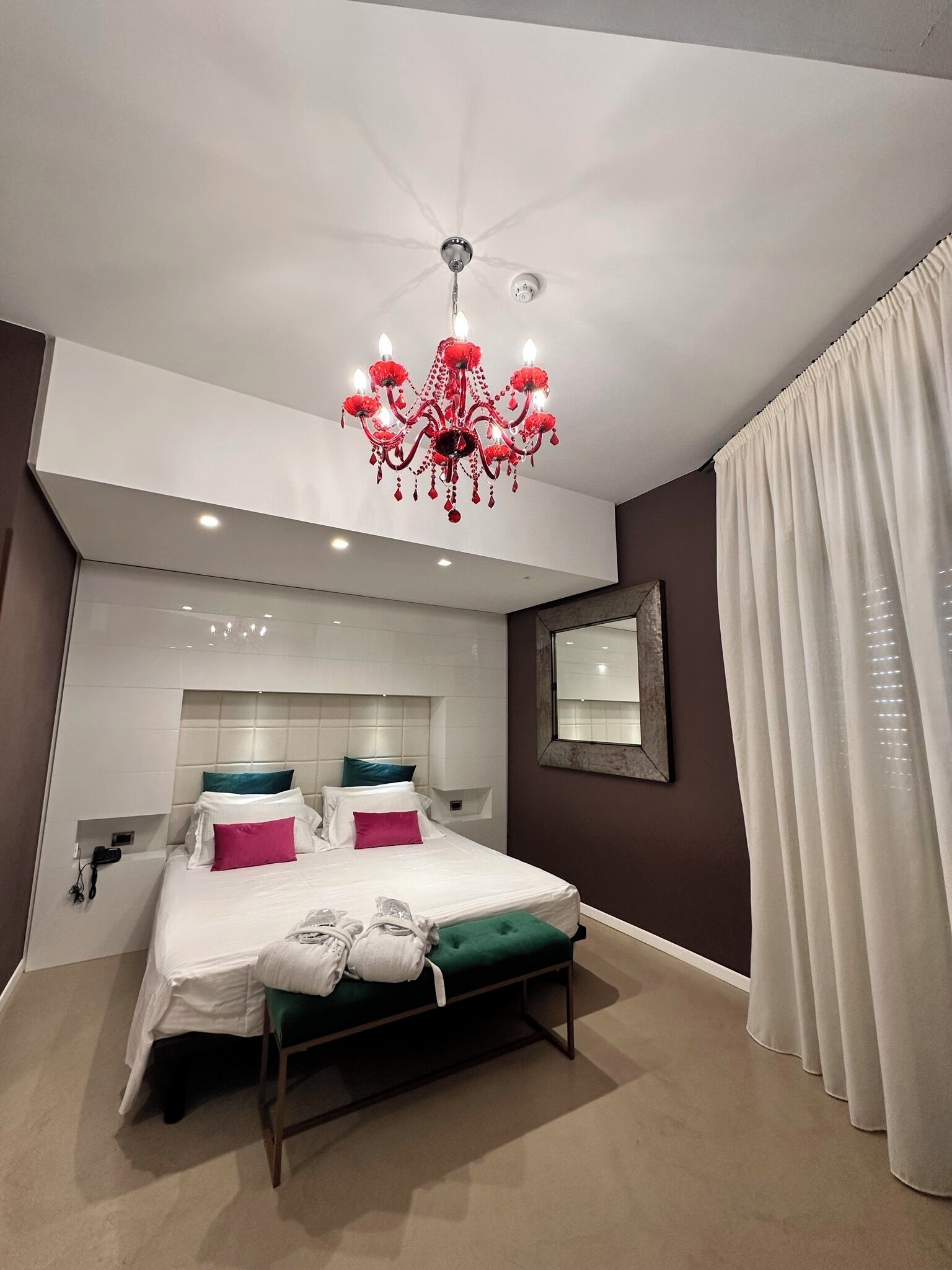 Quarto moderno com uma cama grande, um lustre, uma mesa de cabeceira e um espelho na parede.