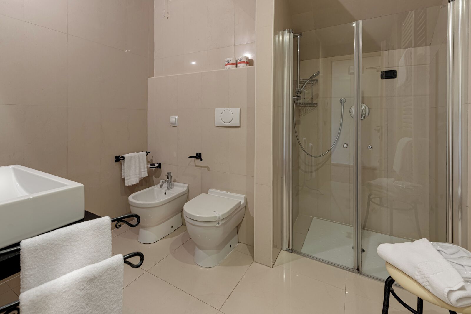 A modern bathroom with a large sink, two bidets, a toilet, and a glass-enclosed shower area.