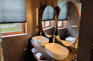 Un baño moderno con dos lavamanos ovalados grandes, un espejo amplio y una ventana.