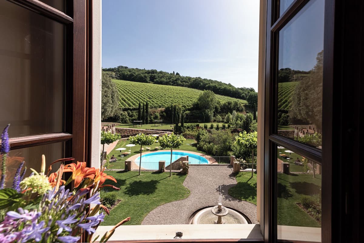 A view from a window overlooking a landscaped garden with a swimming pool and a fountain.