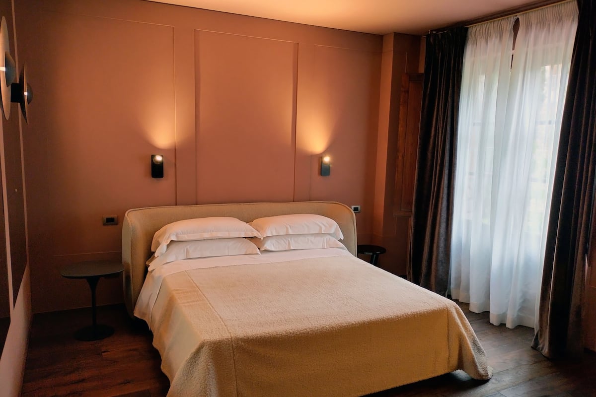 A neatly made bed with white linens, a small bedside table, and wall-mounted lighting.