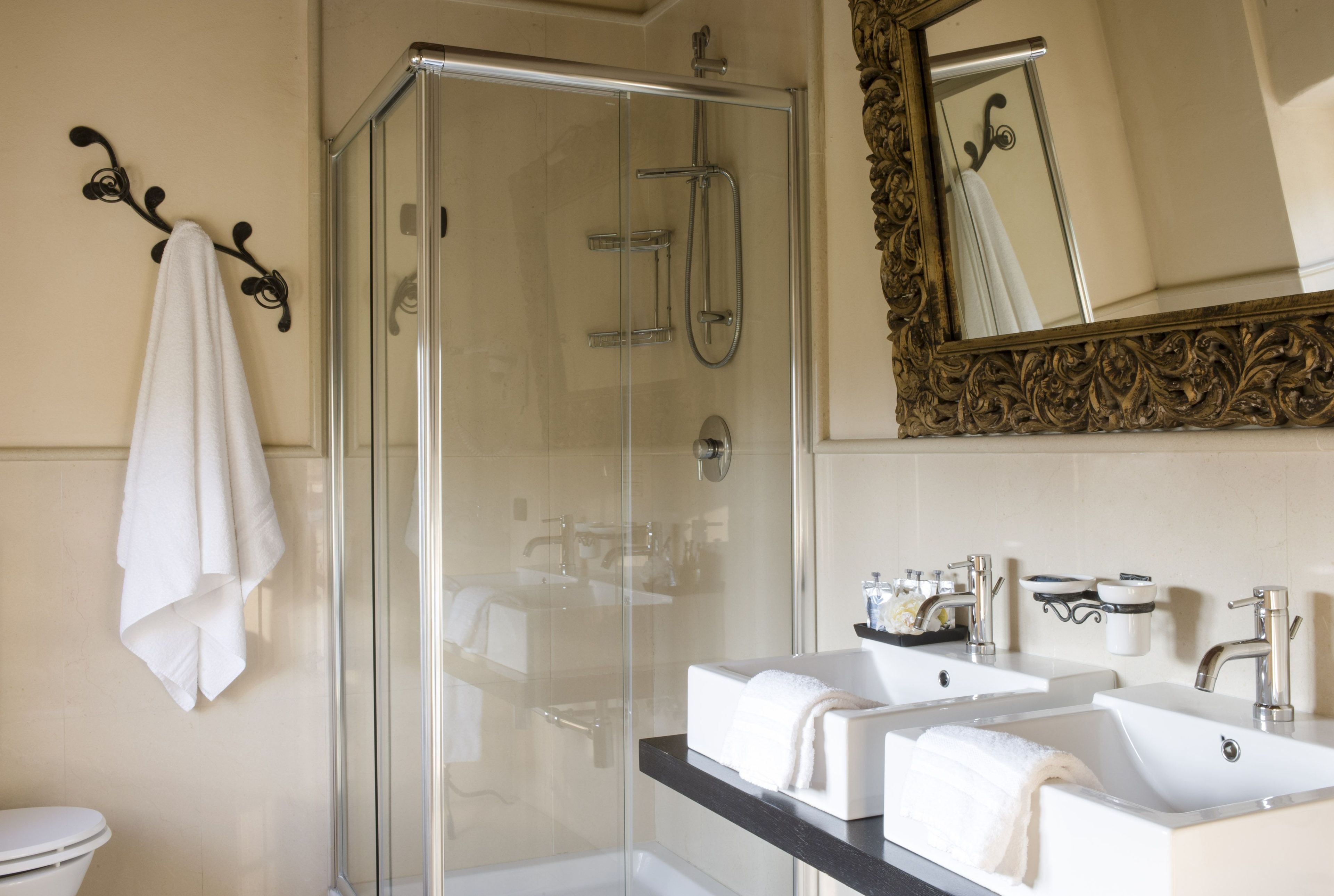 A modern bathroom with a glass-enclosed shower, two sinks with white countertops, and a large mirror with an ornate frame.