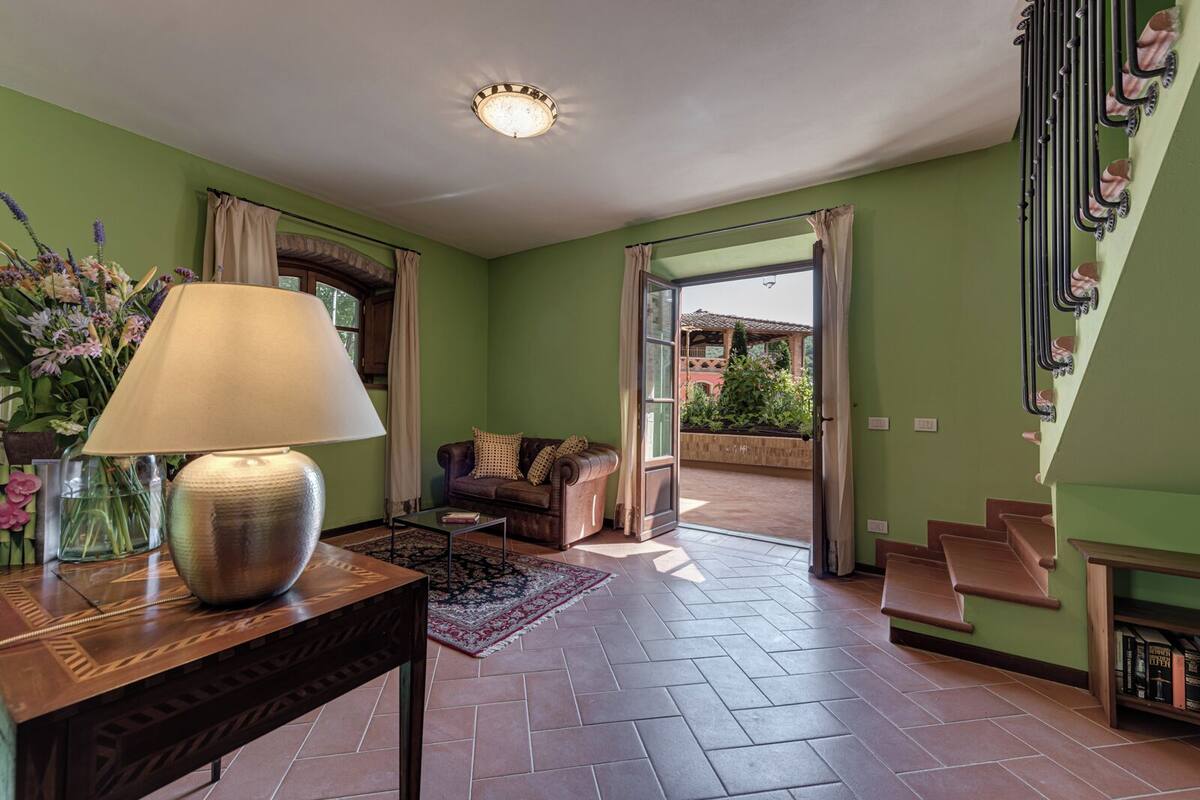 A living room with a sofa, a table with a lamp, a rug, and a staircase leading to an outdoor area.