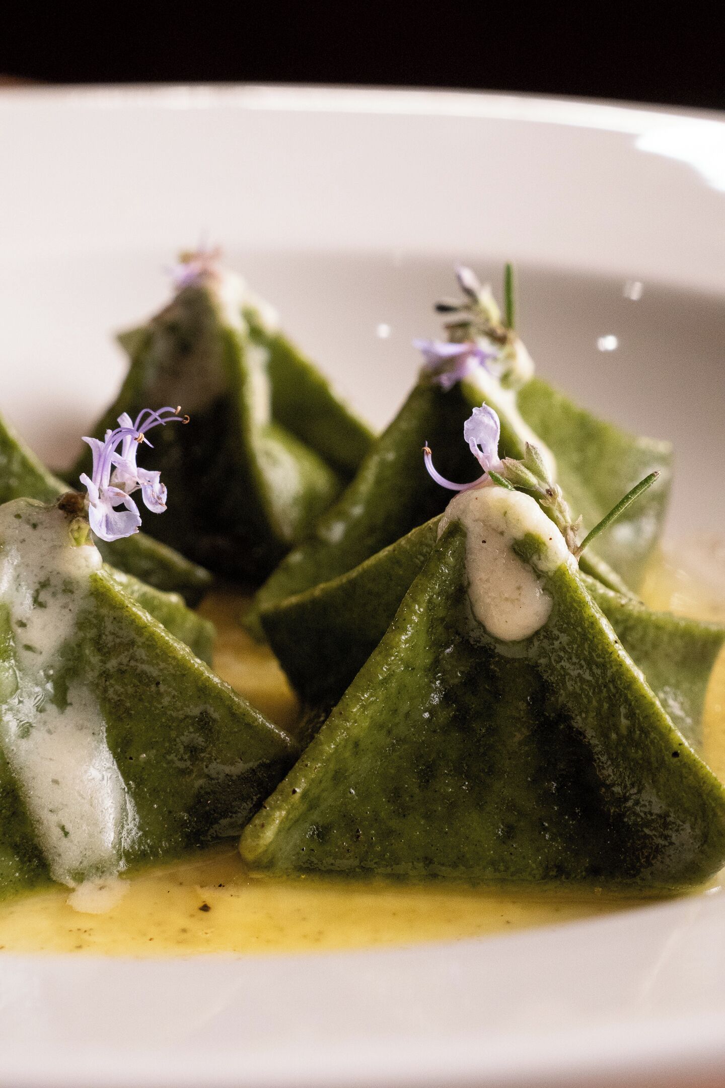 A plate of food with green triangular shapes, possibly a vegetable dish, garnished with small purple flowers and a creamy sauce.