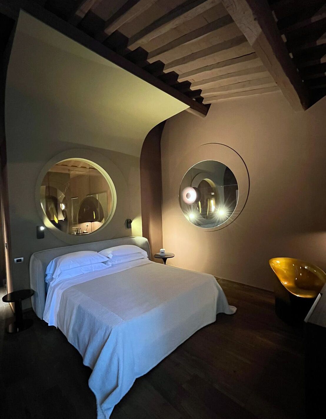 A modern bedroom with a large bed, two round mirrors, a small table, and a unique yellow chair.