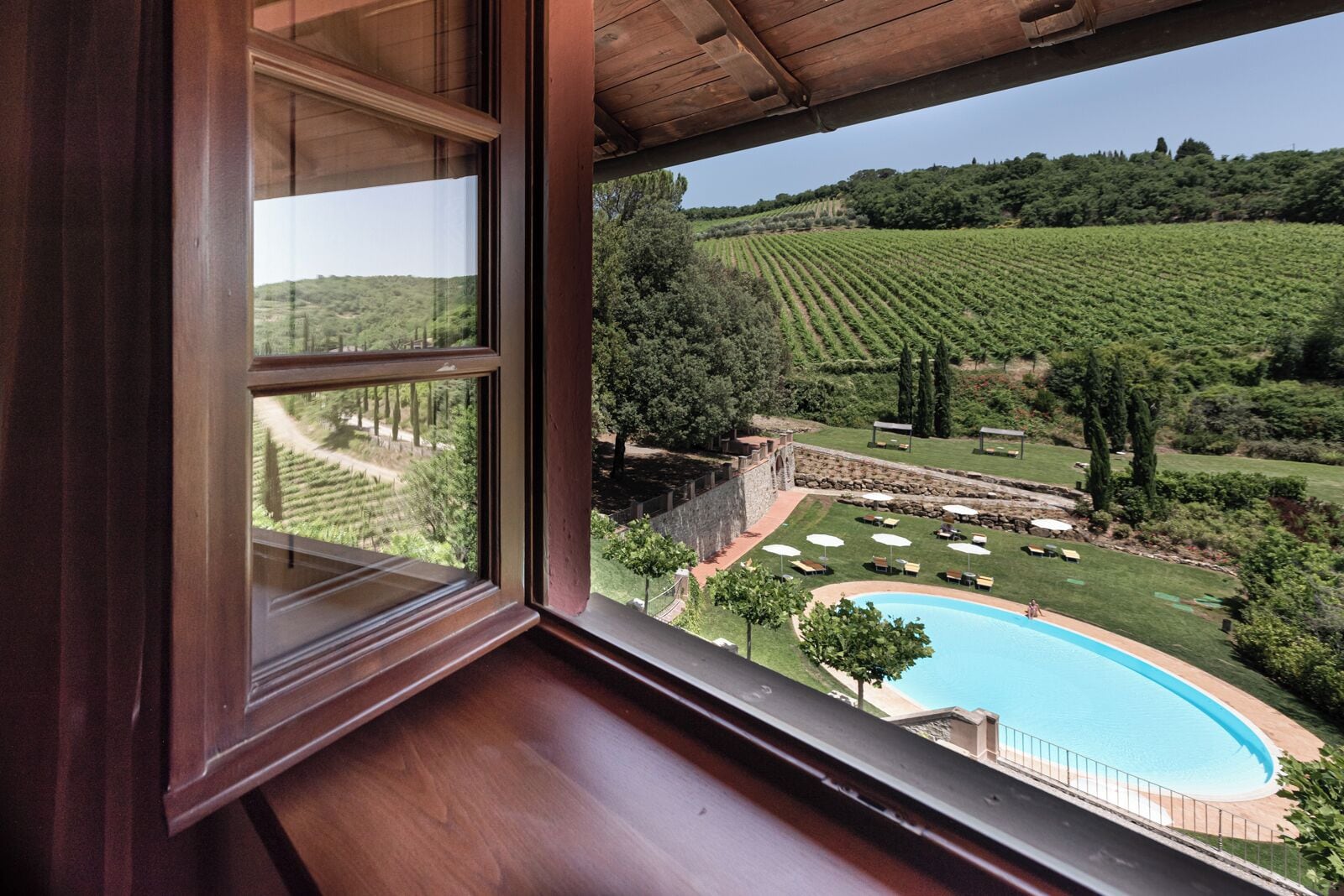 Vista desde una ventana con piscina y viñedo.