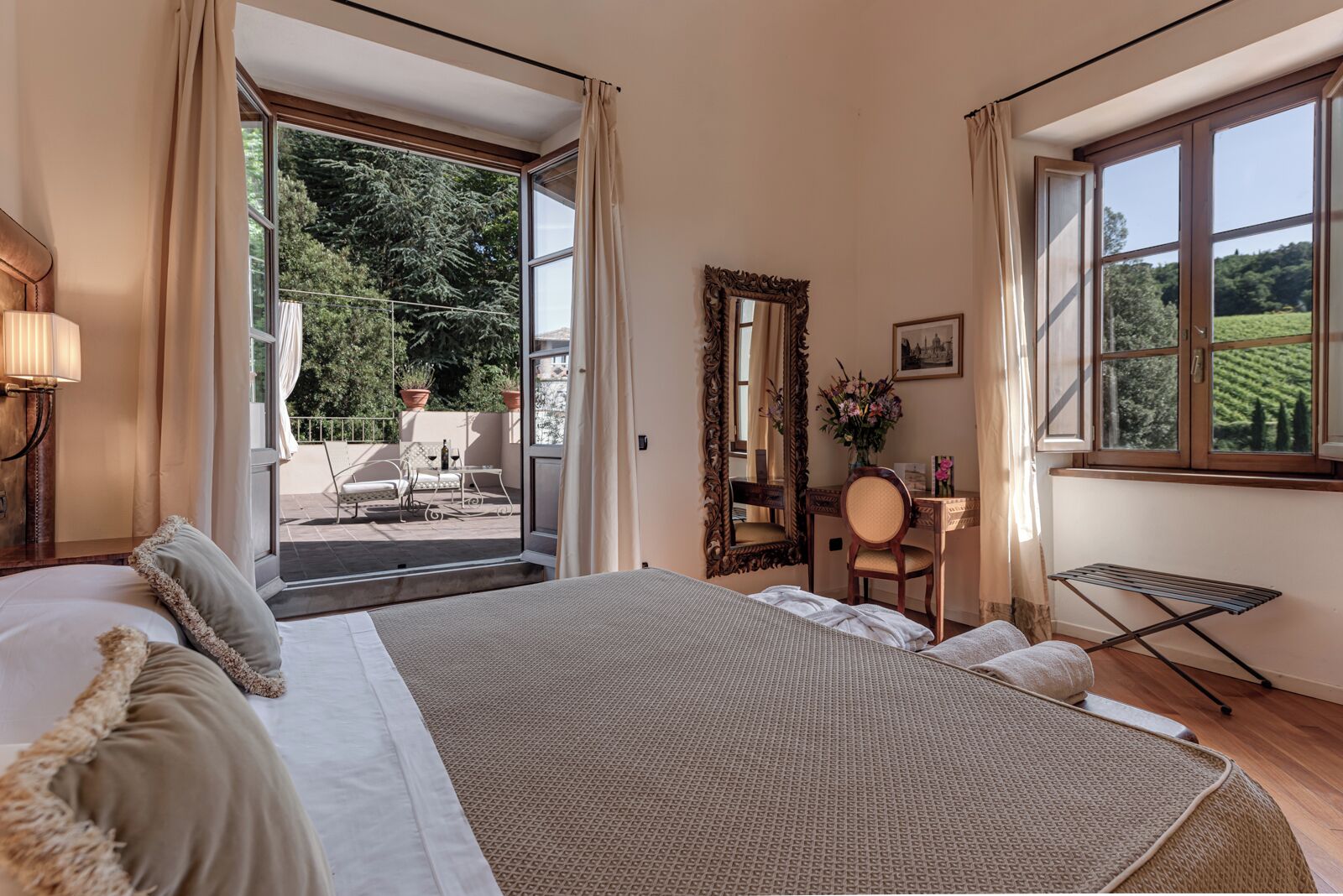 Ein Schlafzimmer mit einem großen Bett, einem Schreibtisch, einem Stuhl, einem Spiegel und Blick auf einen Garten durch das Fenster.