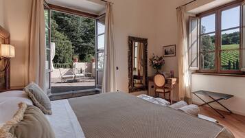 Ein Schlafzimmer mit einem großen Bett, einem Schreibtisch, einem Stuhl, einem Spiegel und Blick auf einen Garten durch das Fenster.