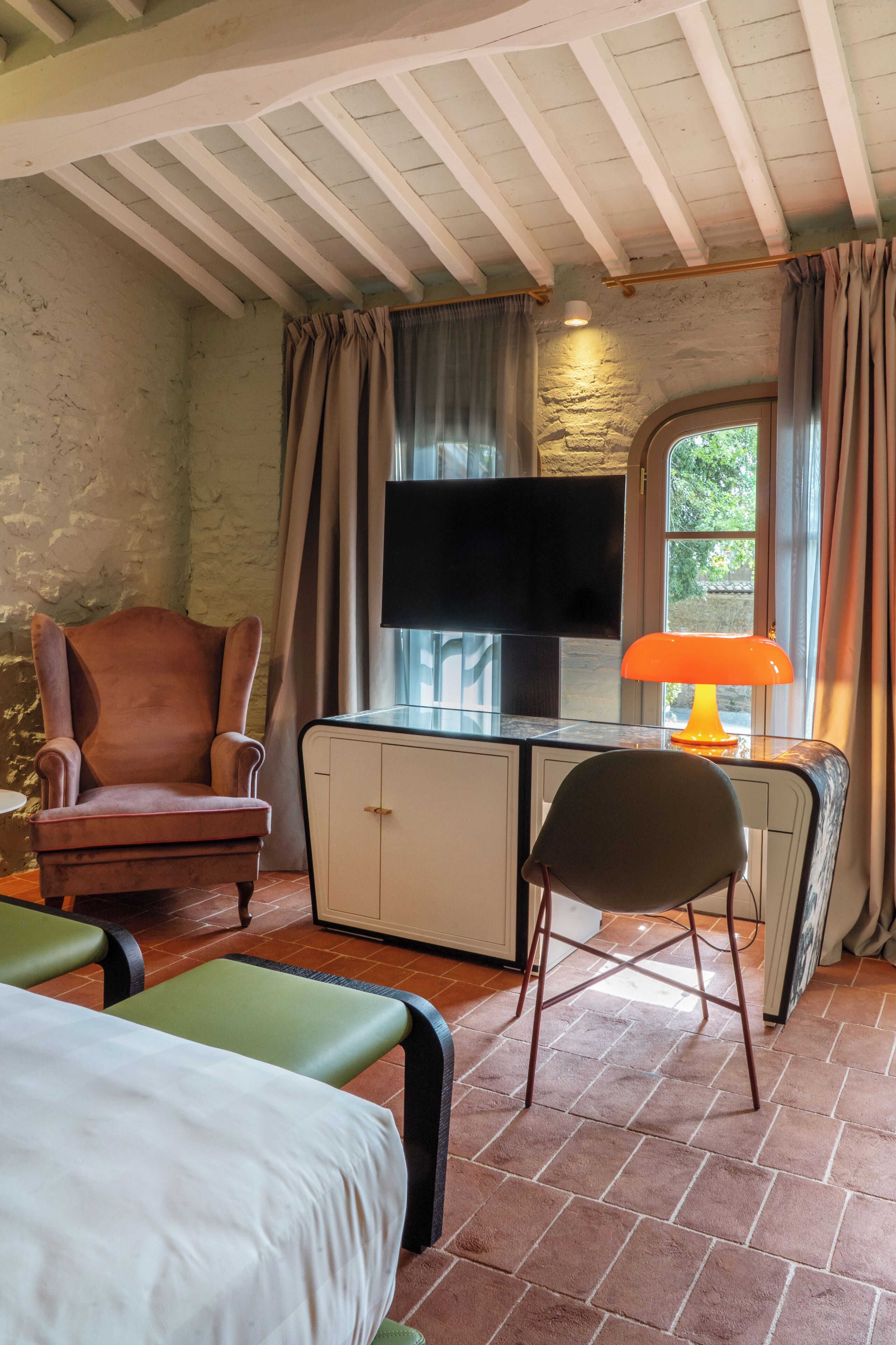 A room with a television, a desk with a lamp, a chair, and a bed.