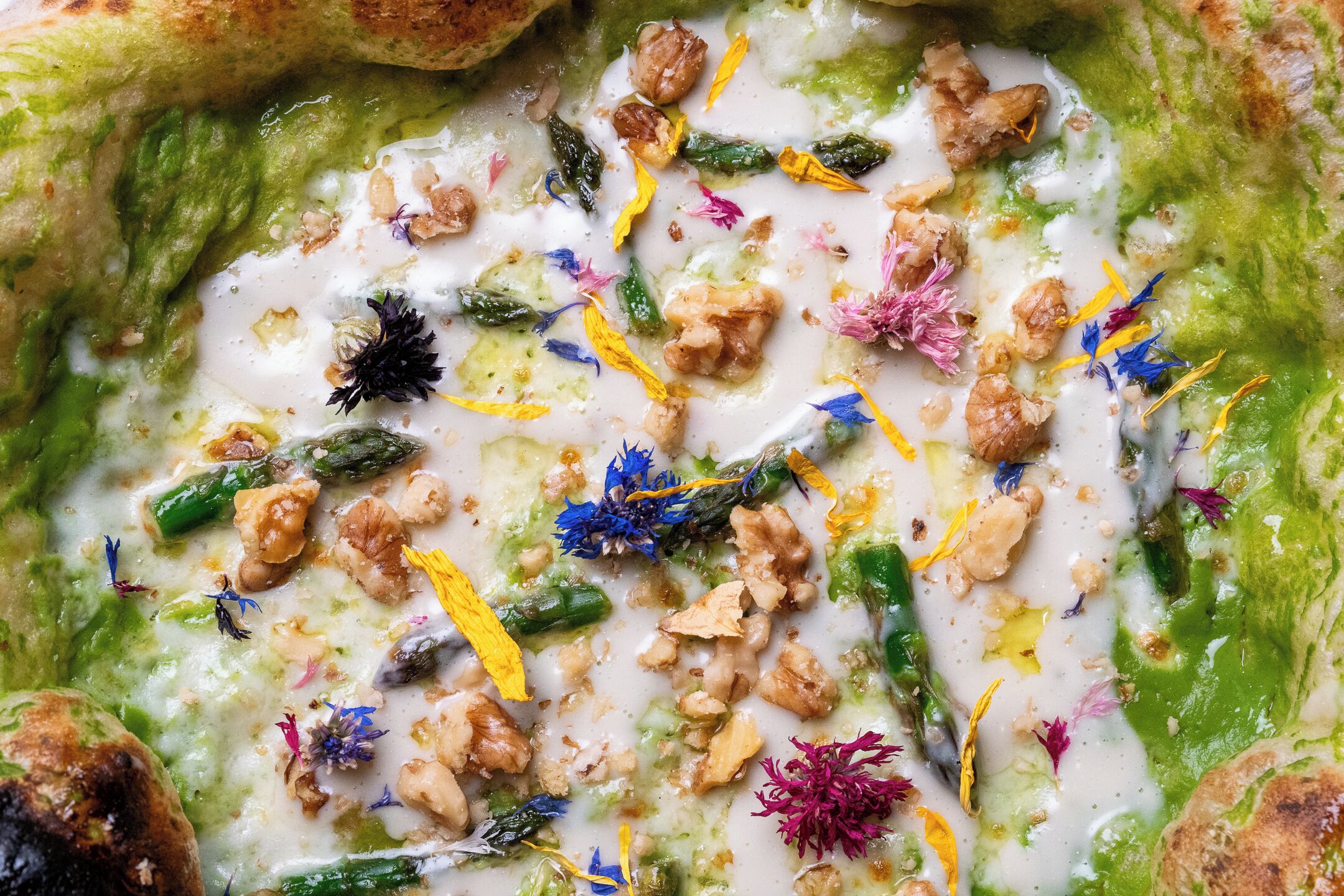 A close-up of a dish with green sauce, nuts, and colorful flower petals.