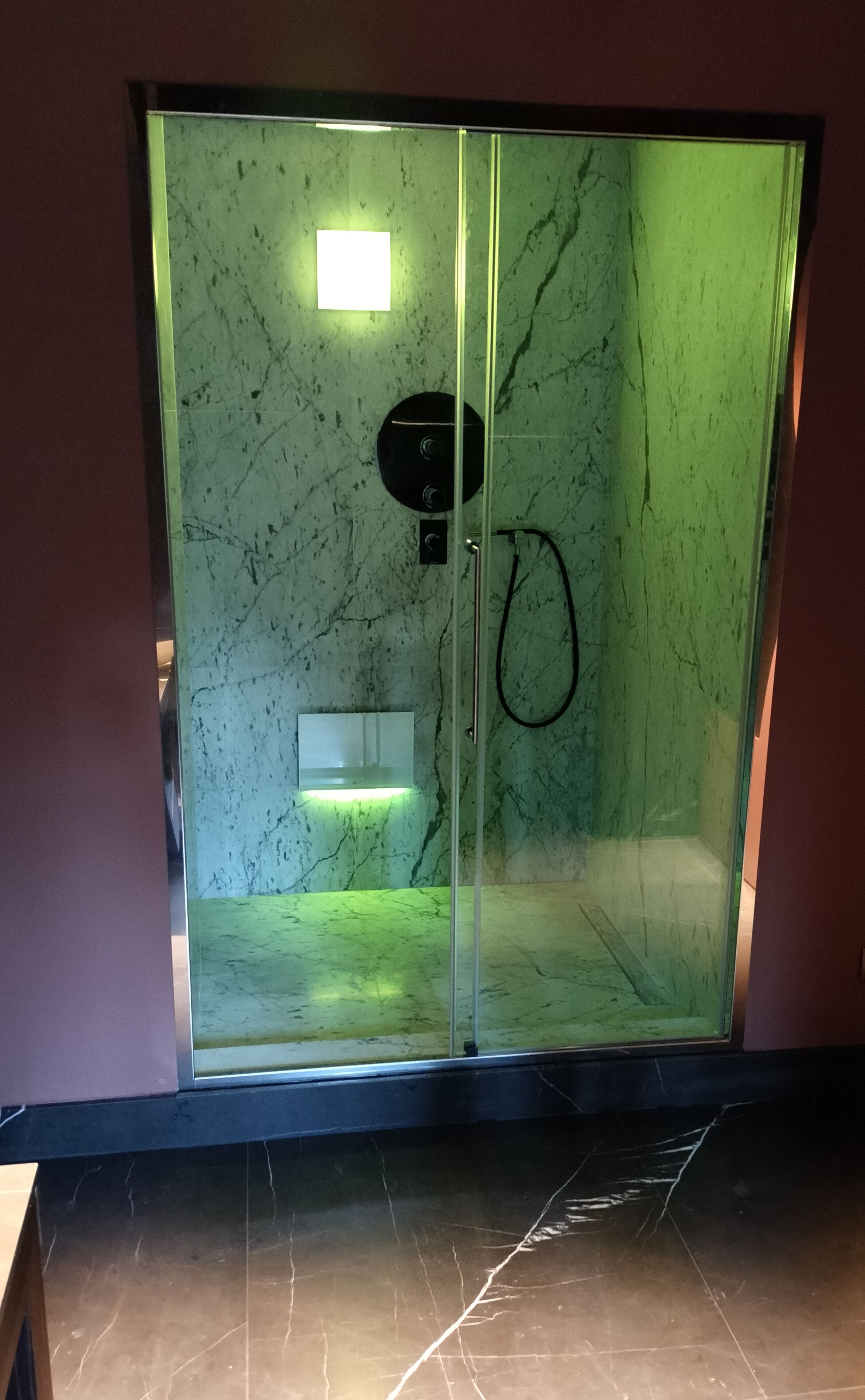 Ducha envuelta en vidrio con panel de control y cabezal de ducha manual.