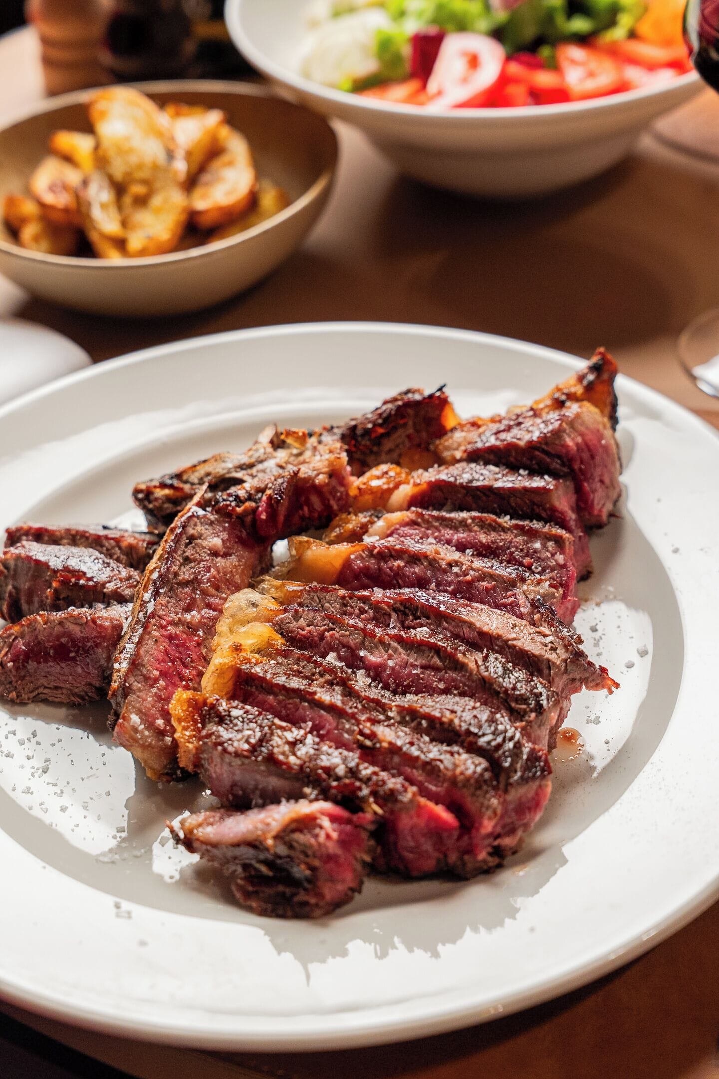 Un plato de carne con patatas asadas y una ensalada.