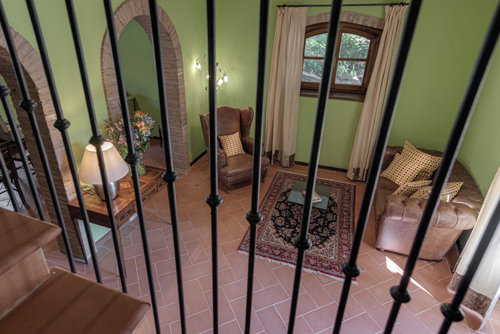 A living room with a brown leather sofa, a patterned rug, and a window with curtains.