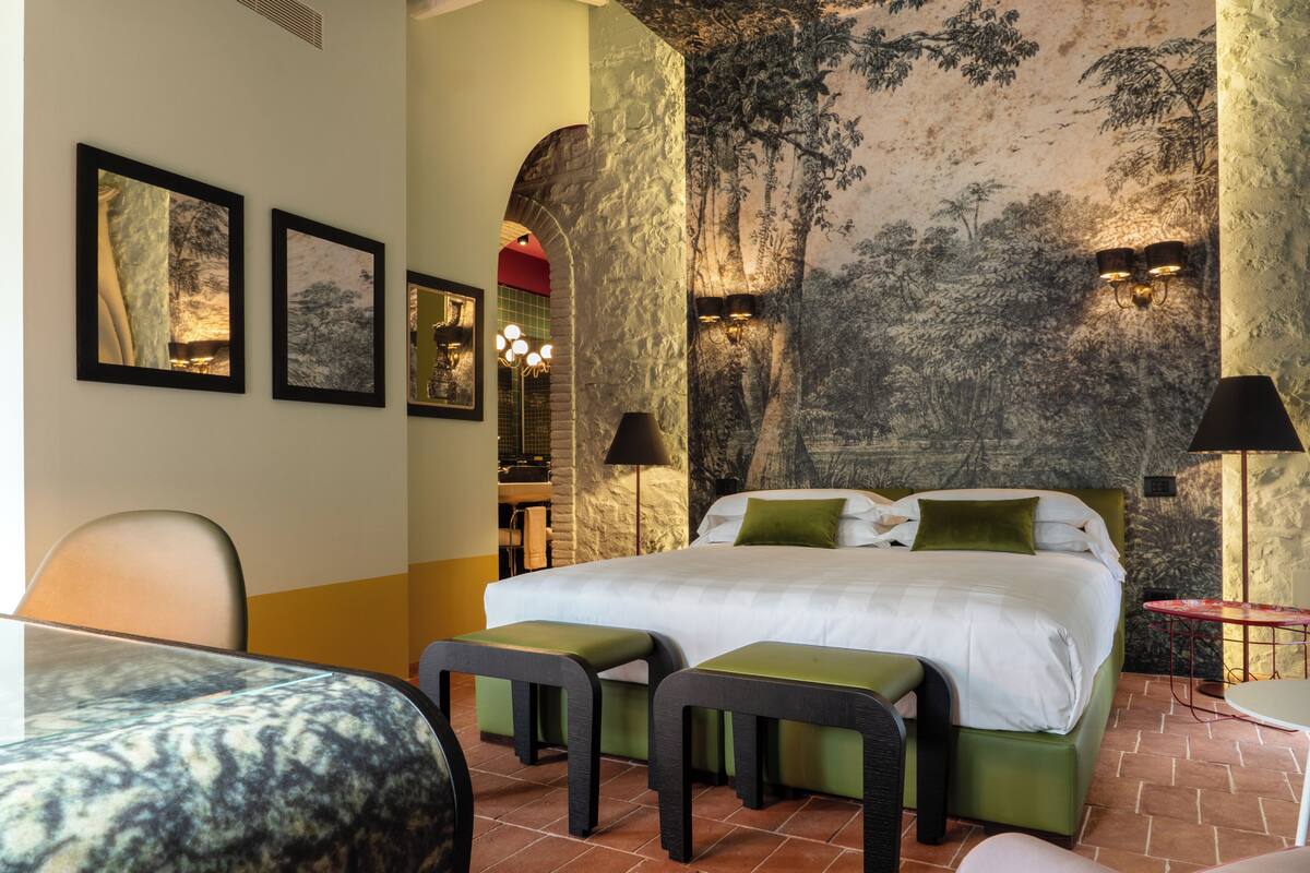 A hotel room with a bed, two bedside tables, a desk, a chair, and a bench.