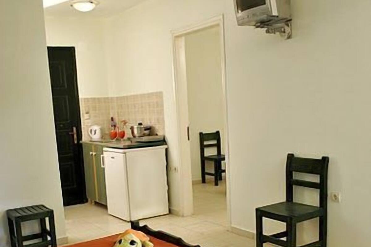 A small, simple room with a bed, a chair, a small table, and a television mounted on the wall.