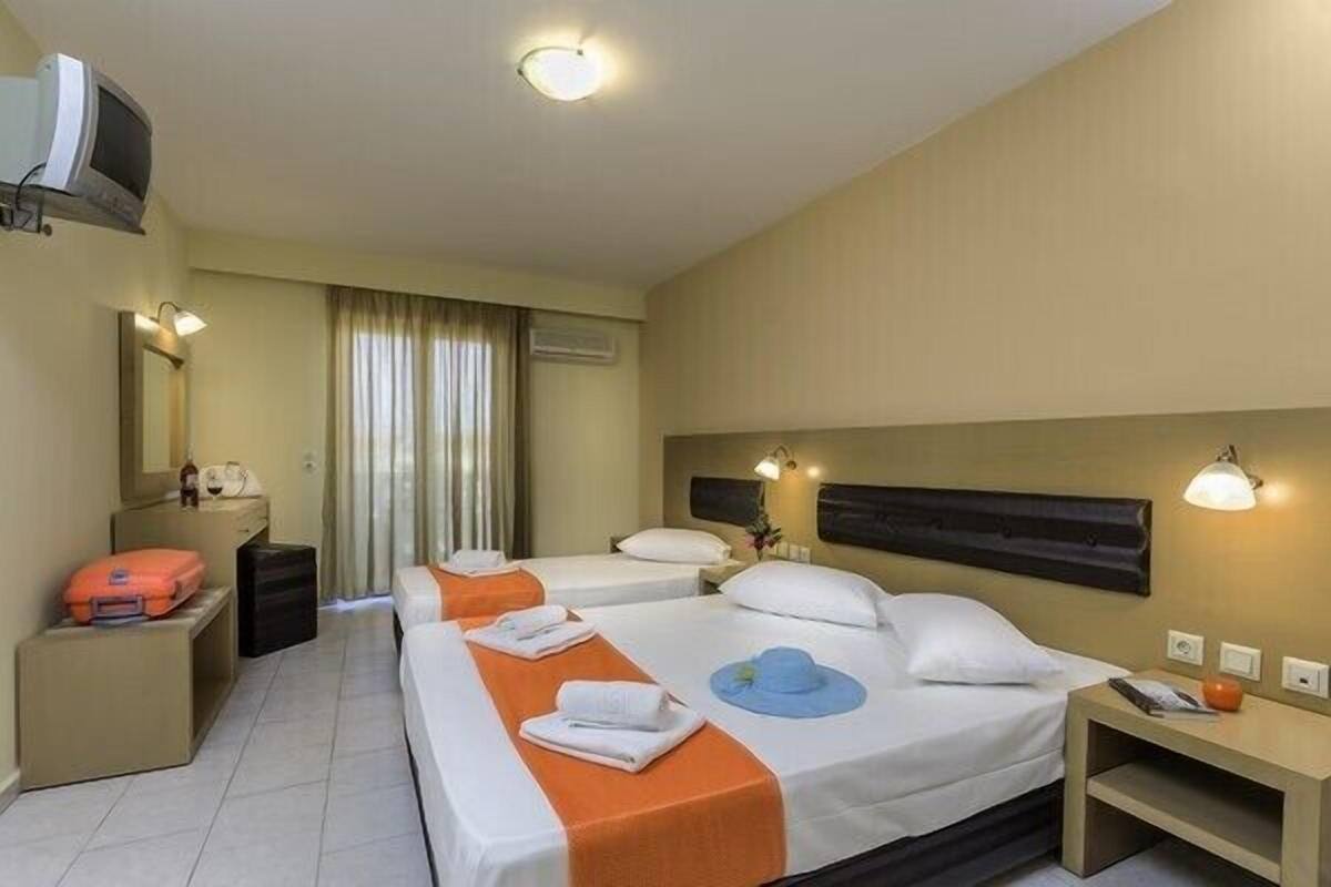 A hotel room with two beds, a desk, a television, and a window with curtains.
