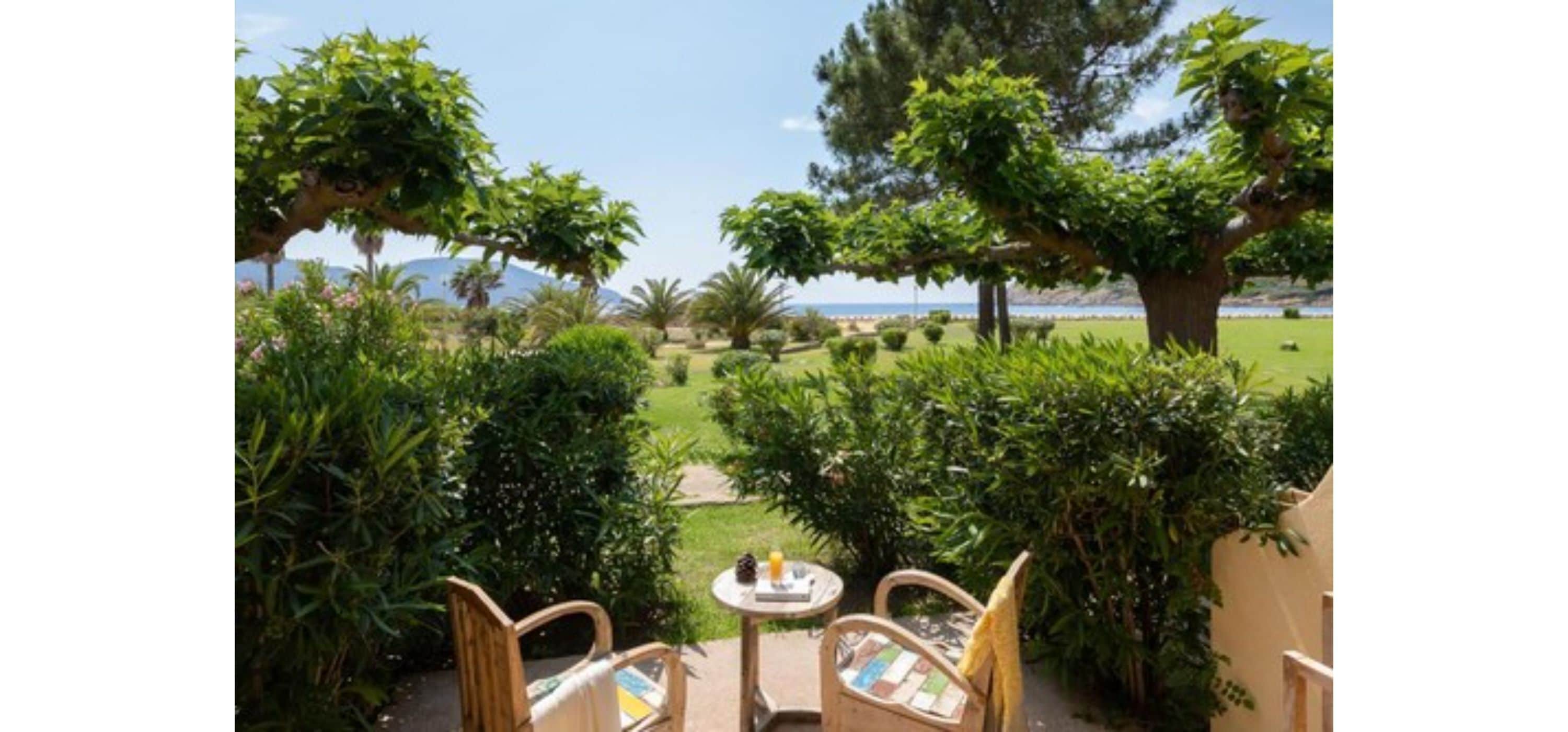 An outdoor seating area with chairs and a table, surrounded by lush greenery and a view of the beach.