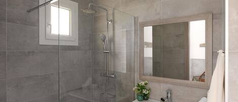 Un baño moderno con ducha envuelta en vidrio, un espejo grande y un lavamanos blanco con un florero.