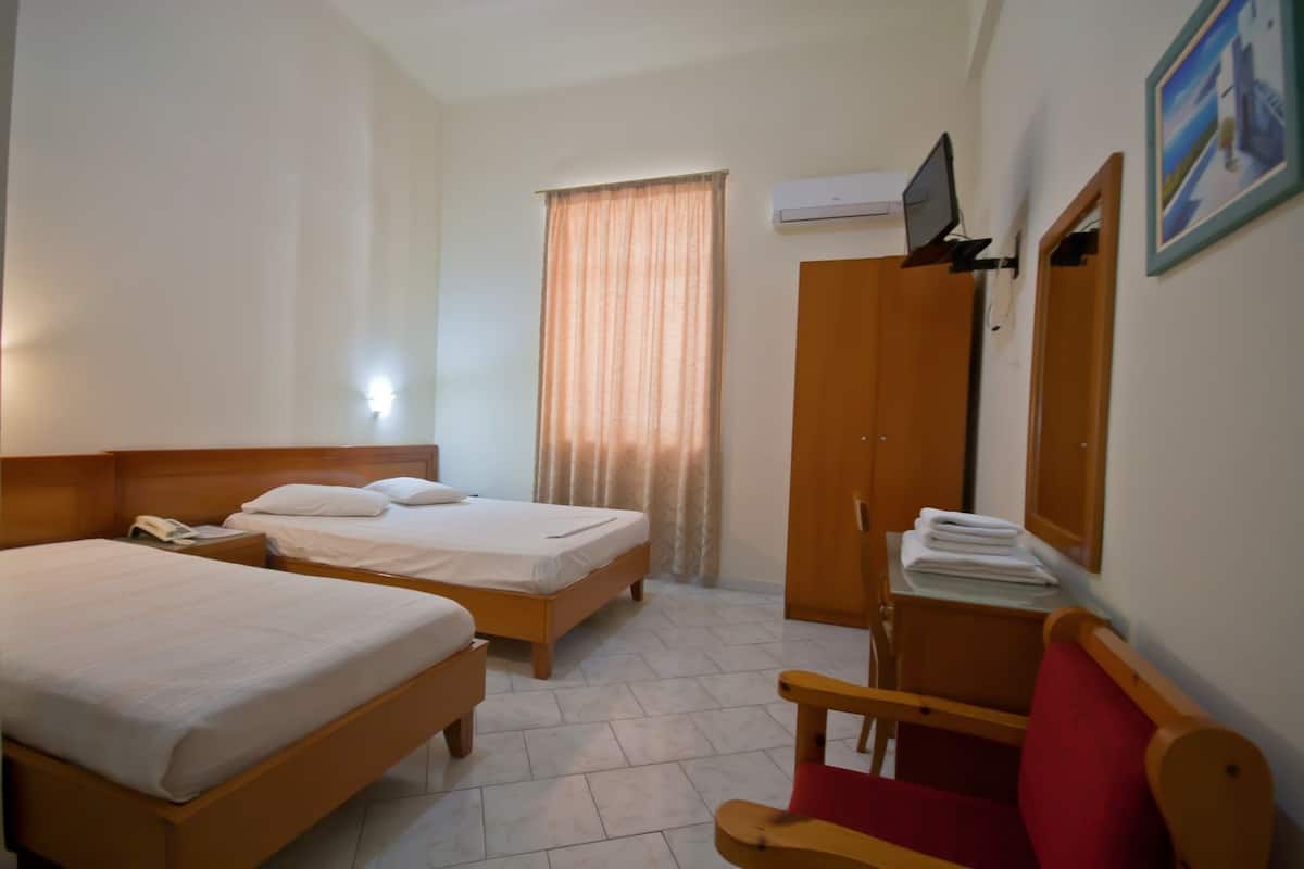 Habitación de hotel con dos camas, un escritorio, una silla, aire acondicionado y una ventana con cortinas.