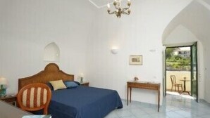 A bedroom with a bed, a chair, a small table, a chandelier, and a view of the outside. - Il Ducato di Ravello (Ravello)
