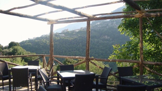 An outdoor seating area with tables and chairs, surrounded by a wooden pergola, overlooking a mountainous landscape. - Il Ducato di Ravello (Ravello)