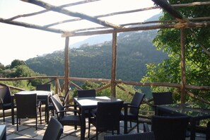 An outdoor seating area with tables and chairs, surrounded by a wooden pergola, overlooking a mountainous landscape. - Il Ducato di Ravello (Ravello)